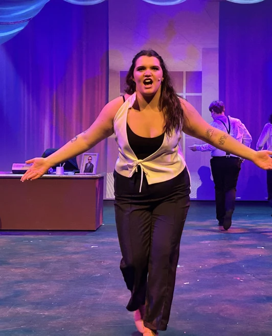 Performer delivering a powerful monologue, surrounded by other actors on stage in dramatic poses. Performer delivering a powerful monologue, surrounded by other actors on stage in dramatic poses.